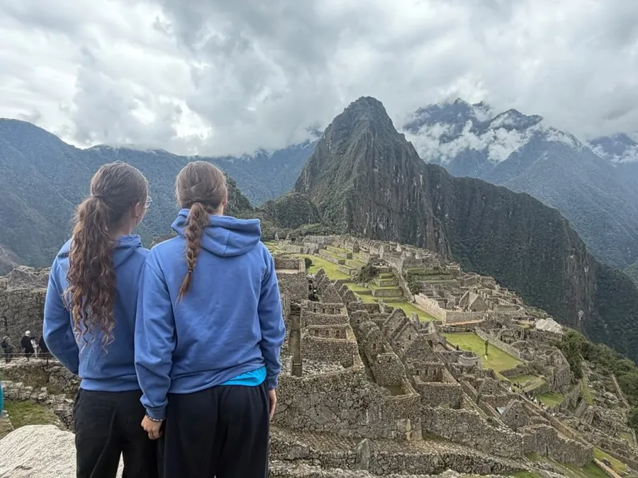 The two sisters, seen from behind in blue hoodies, looking out over the ruins of Machu Picchu