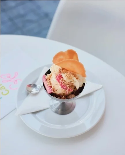 Ice cream in a metal sundae cup topped with a wafer, on a white plate with a spoon at the River Cafe Cafe