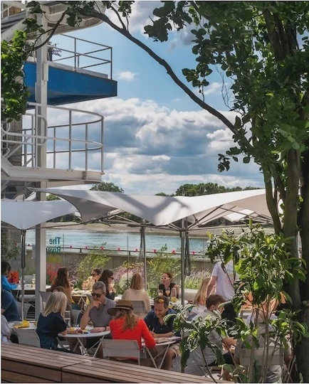 People eating at tables under white canopies on the River Cafe Cafe terrace, with the Thames behind