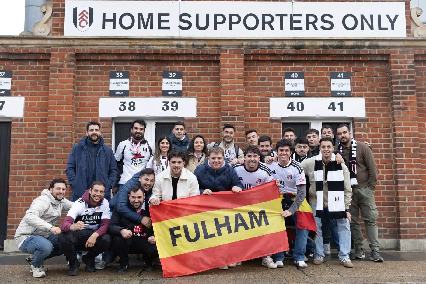 The group crouching with their Fulham banner beneath a Home Supporters Only sign at the turnstiles
