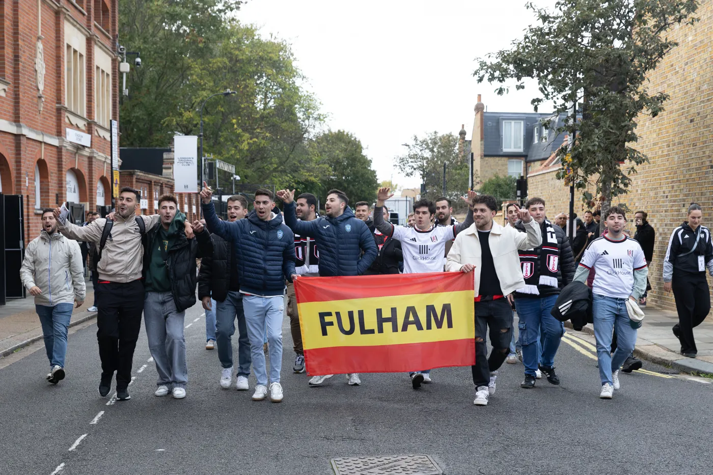 Members of the group walk along the road outside Craven Cottage carrying a red and yellow Fulham banner