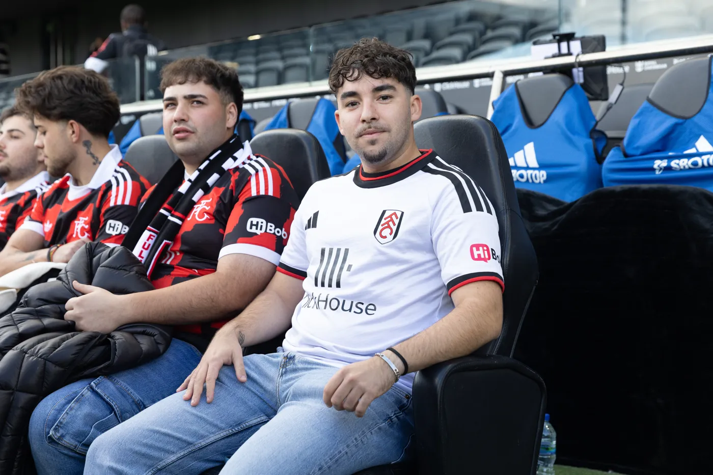 Two fans from the group sitting in the padded dugout seats at Craven Cottage