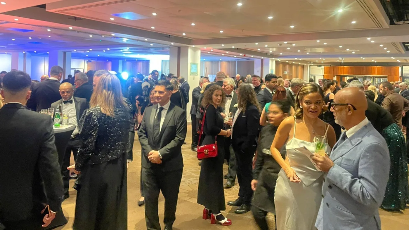 Guests in black tie and evening dresses talking with drinks in a large function room