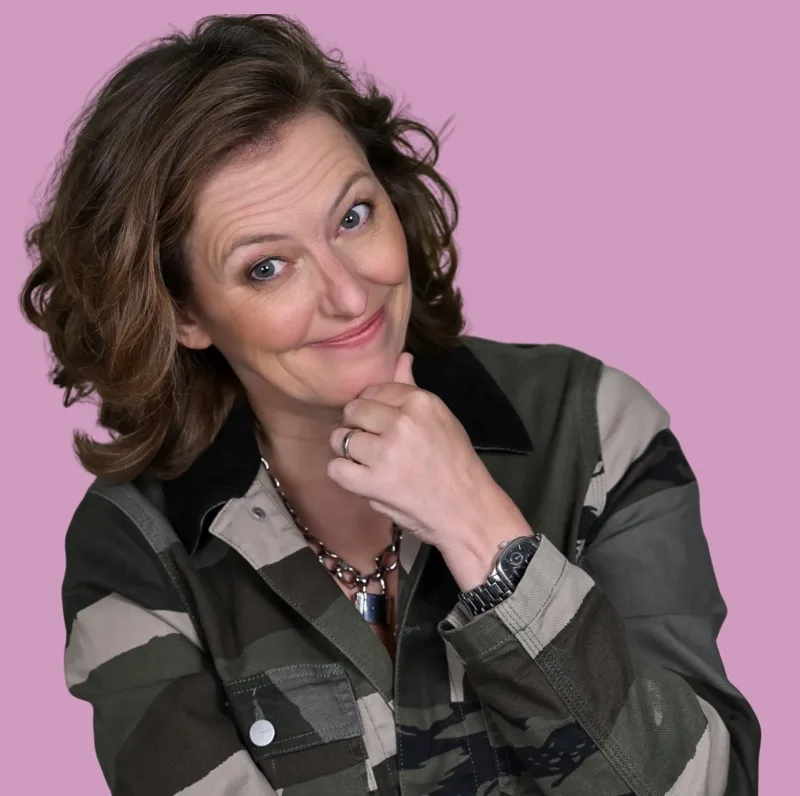 Rosie Wilby, smiling with her chin on her hand, against a pink background