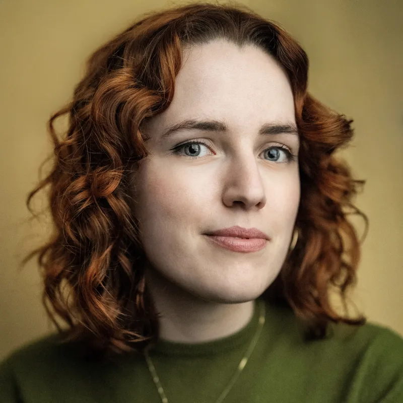 Portrait of Angela Channell, who has curly red hair and wears a green jumper
