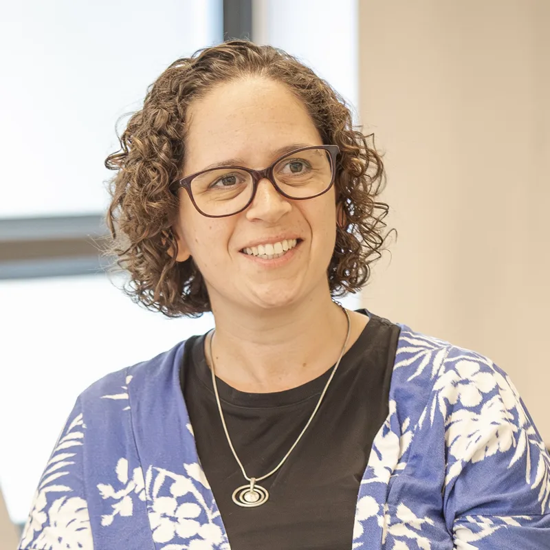Sarah Forbes, wearing glasses and a blue patterned top, smiling