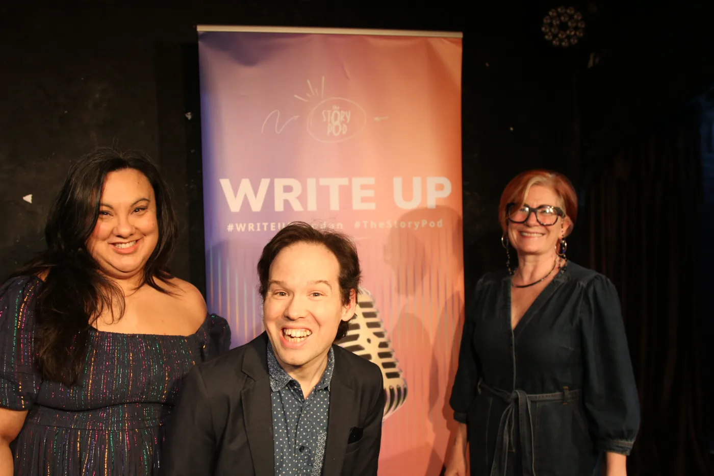 Three people beside a WRITE UP banner on a stage